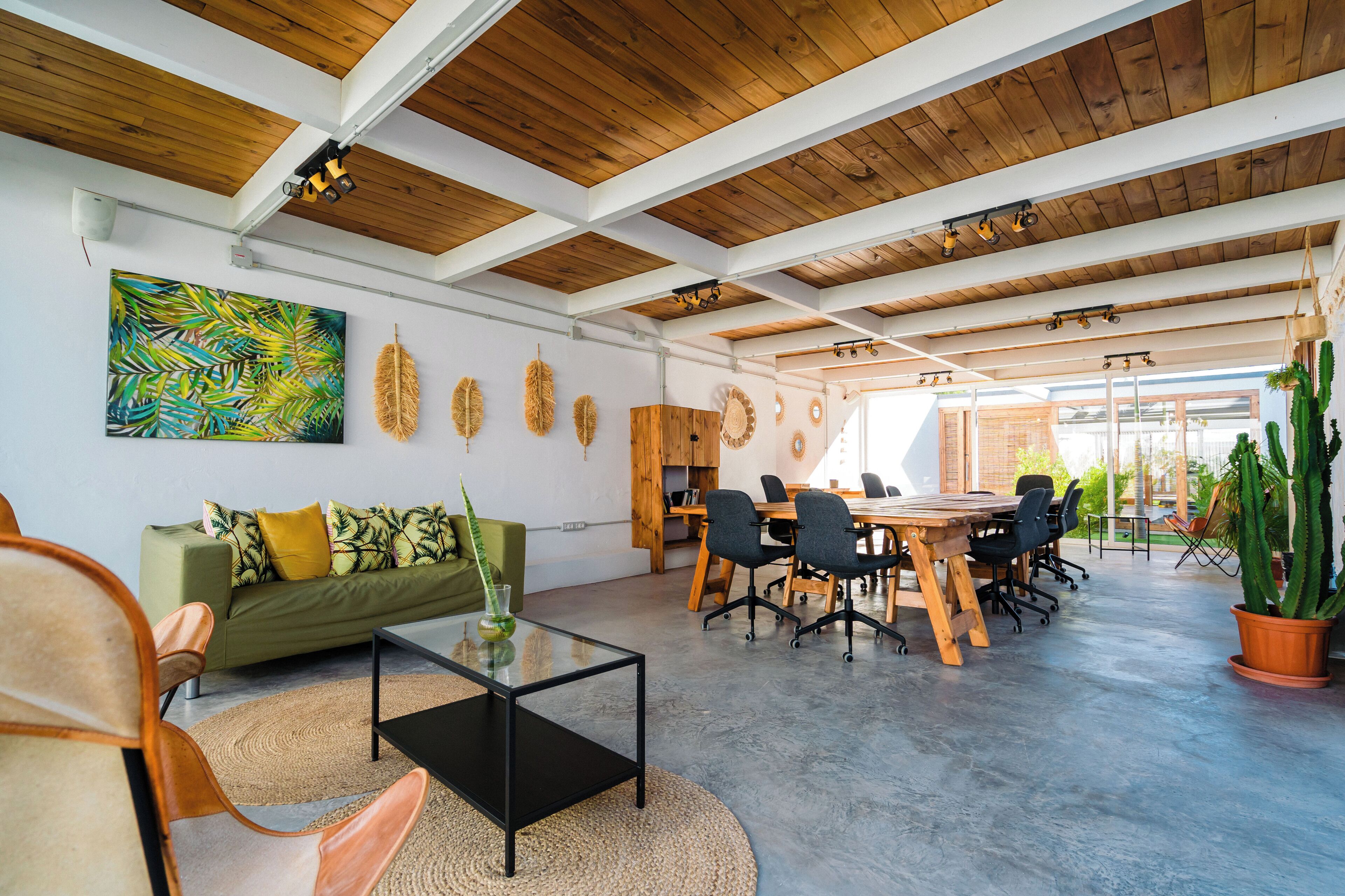 Amplia habitación con techo de madera, un sofá verde, una mesa de centro de vidrio y una zona de comedor con mesa y sillas de madera.