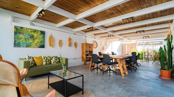Amplia habitación con techo de madera, un sofá verde, una mesa de centro de vidrio y una zona de comedor con mesa y sillas de madera.