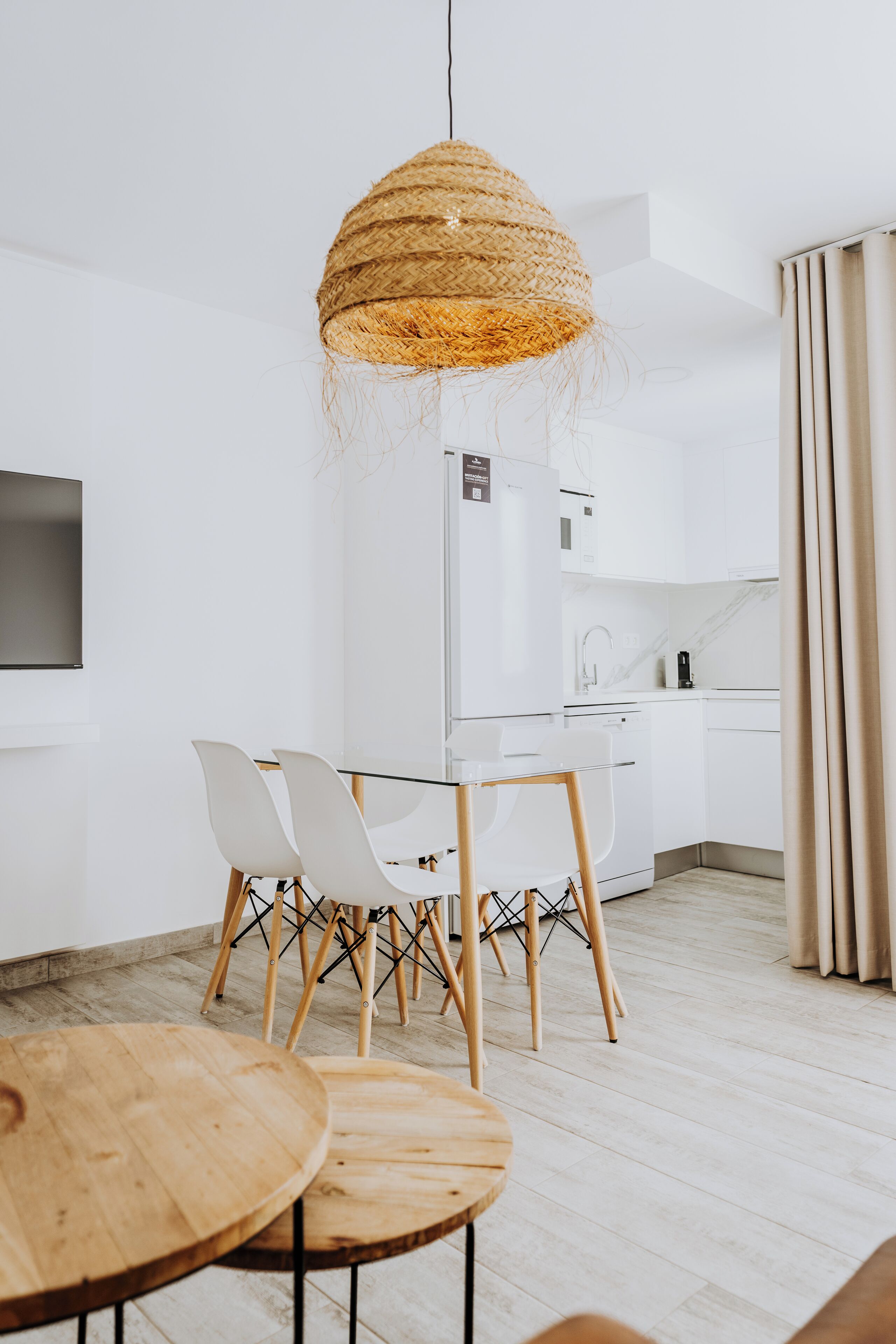 Une cuisine moderne avec des meubles blancs, un four encastré et un coin repas comprenant une table et des chaises en verre.