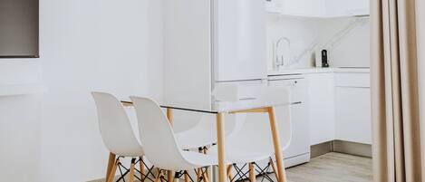 A modern kitchen with white cabinets, a built-in oven, and a dining area with a glass table and chairs.