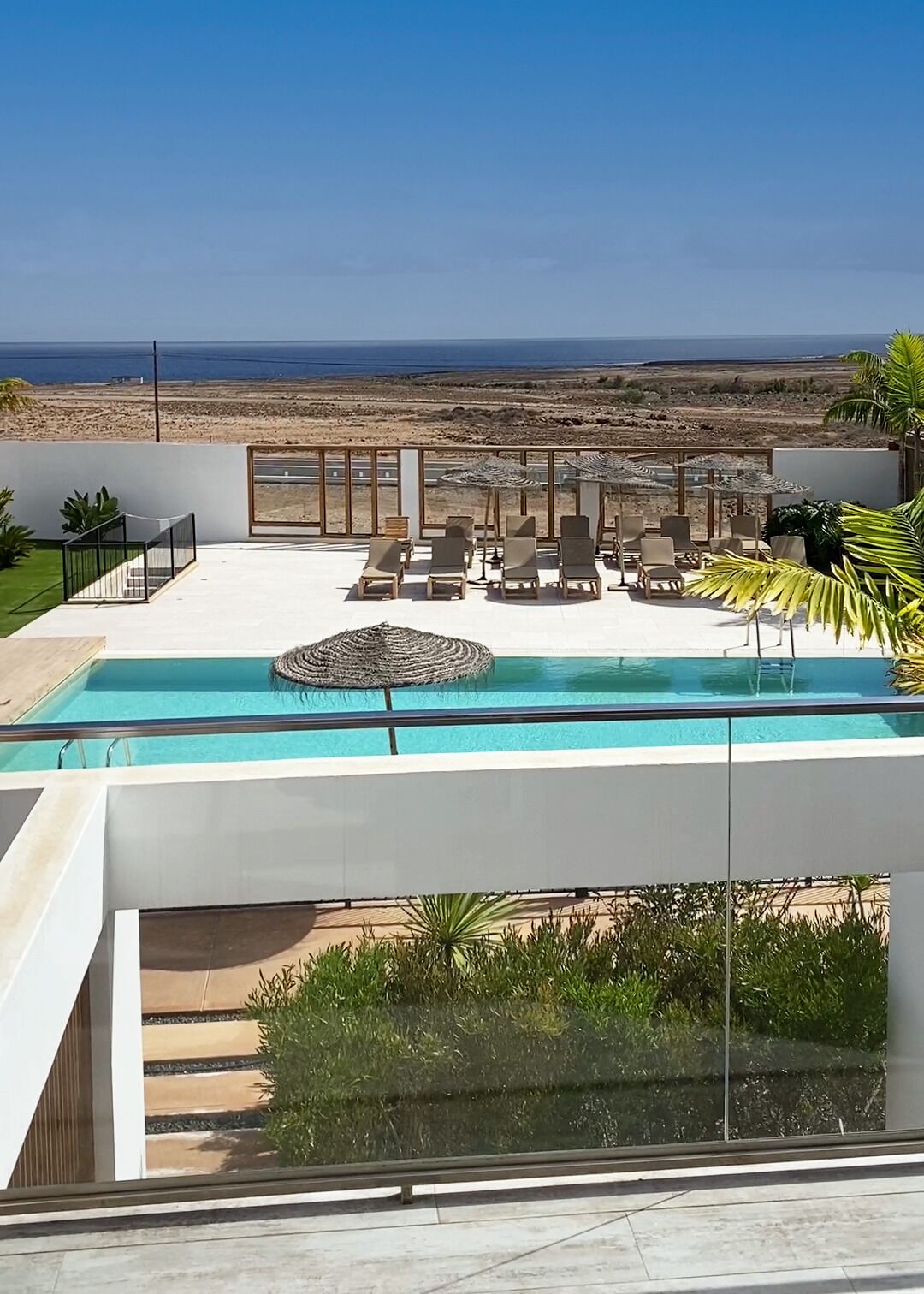 A modern outdoor pool area with lounge chairs and umbrellas, overlooking a desert landscape.