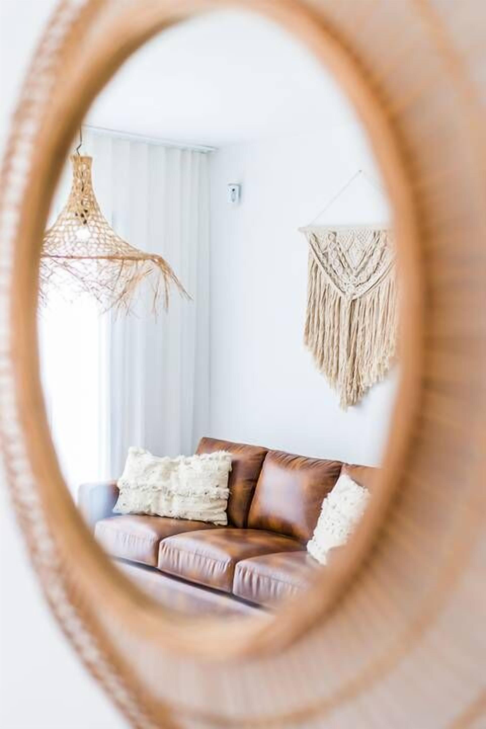 Une pièce avec un canapé en cuir marron, un luminaire suspendu en fibres tressées et une décoration murale en macramé.