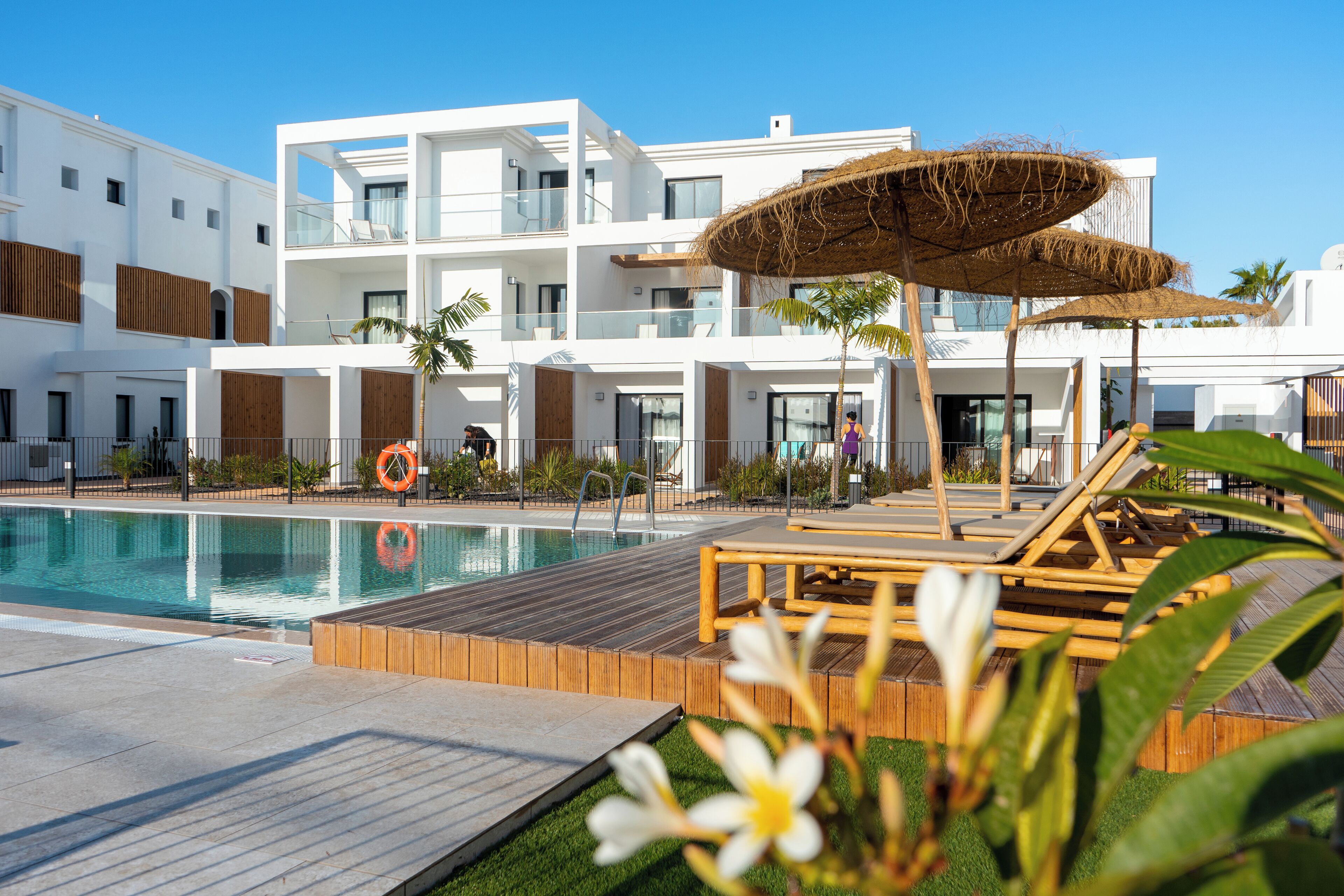 Un hotel moderno con piscina, terraza de madera y sillones de descanso.