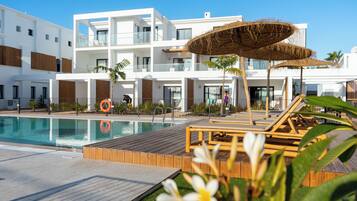 Un hotel moderno con piscina, terraza de madera y sillones de descanso.
