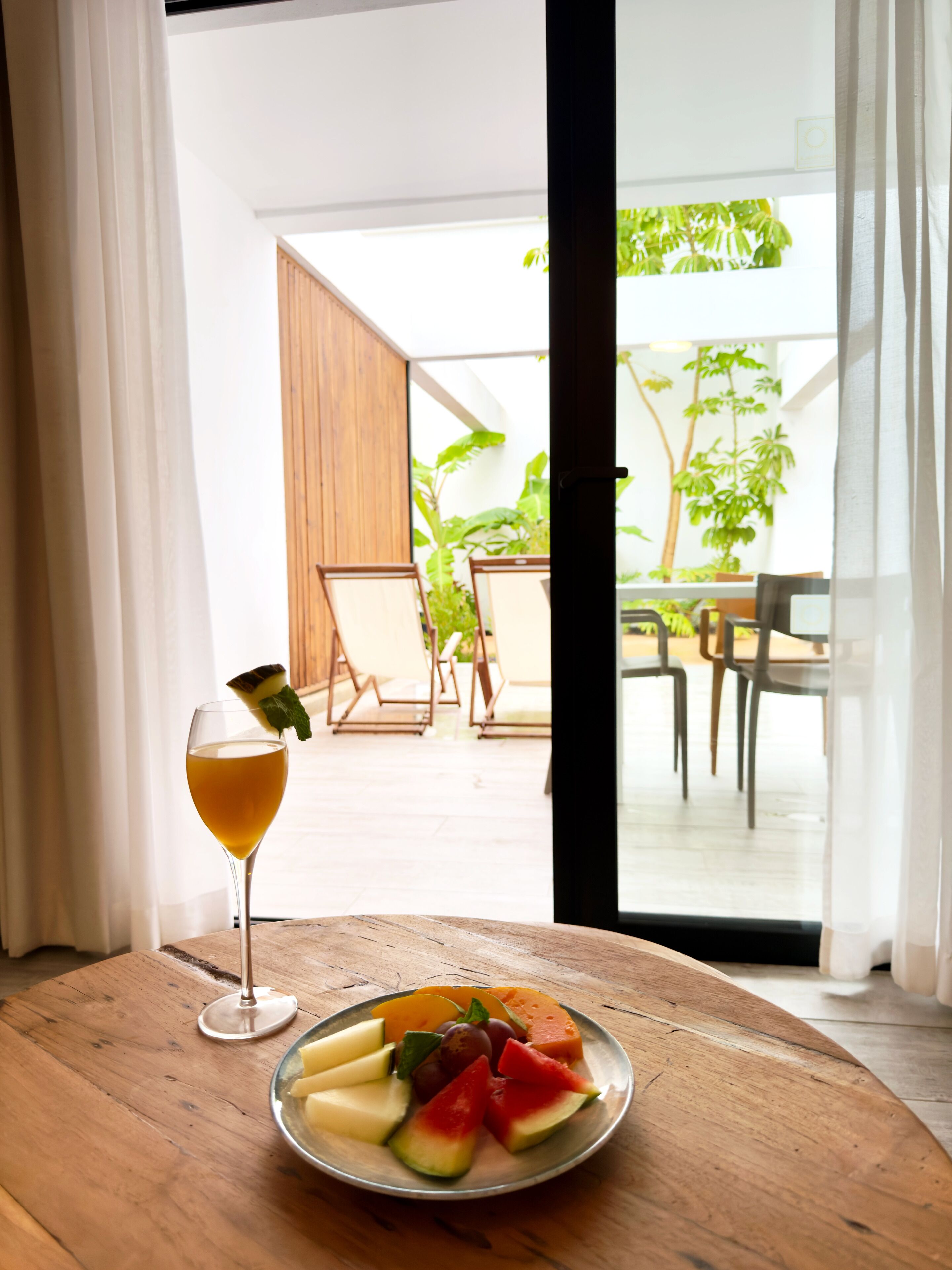 Uma área de refeições com uma mesa, um copo de bebida e uma travessa de frutas.