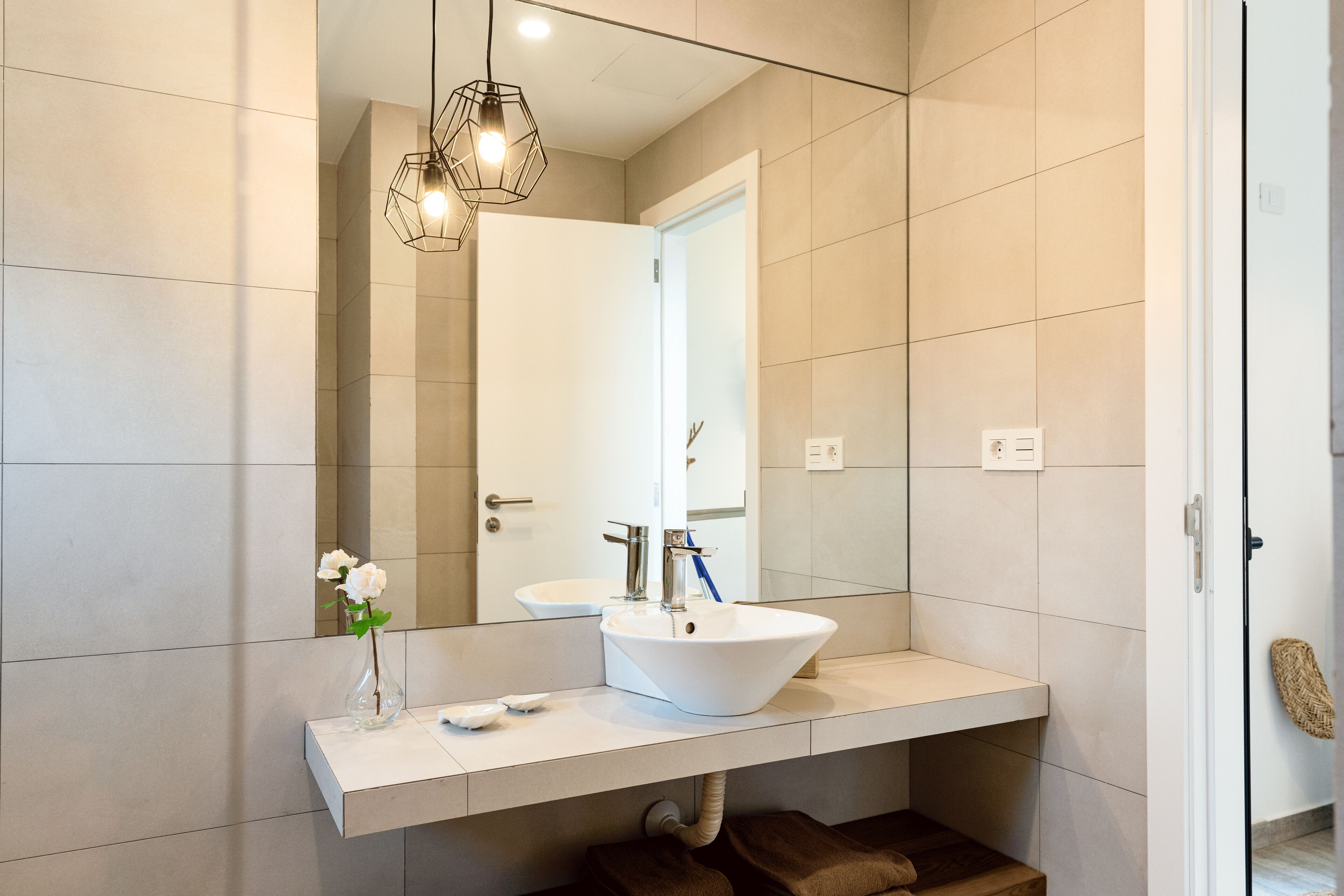 Une salle de bain moderne avec un lavabo blanc, un miroir et un luminaire suspendu.