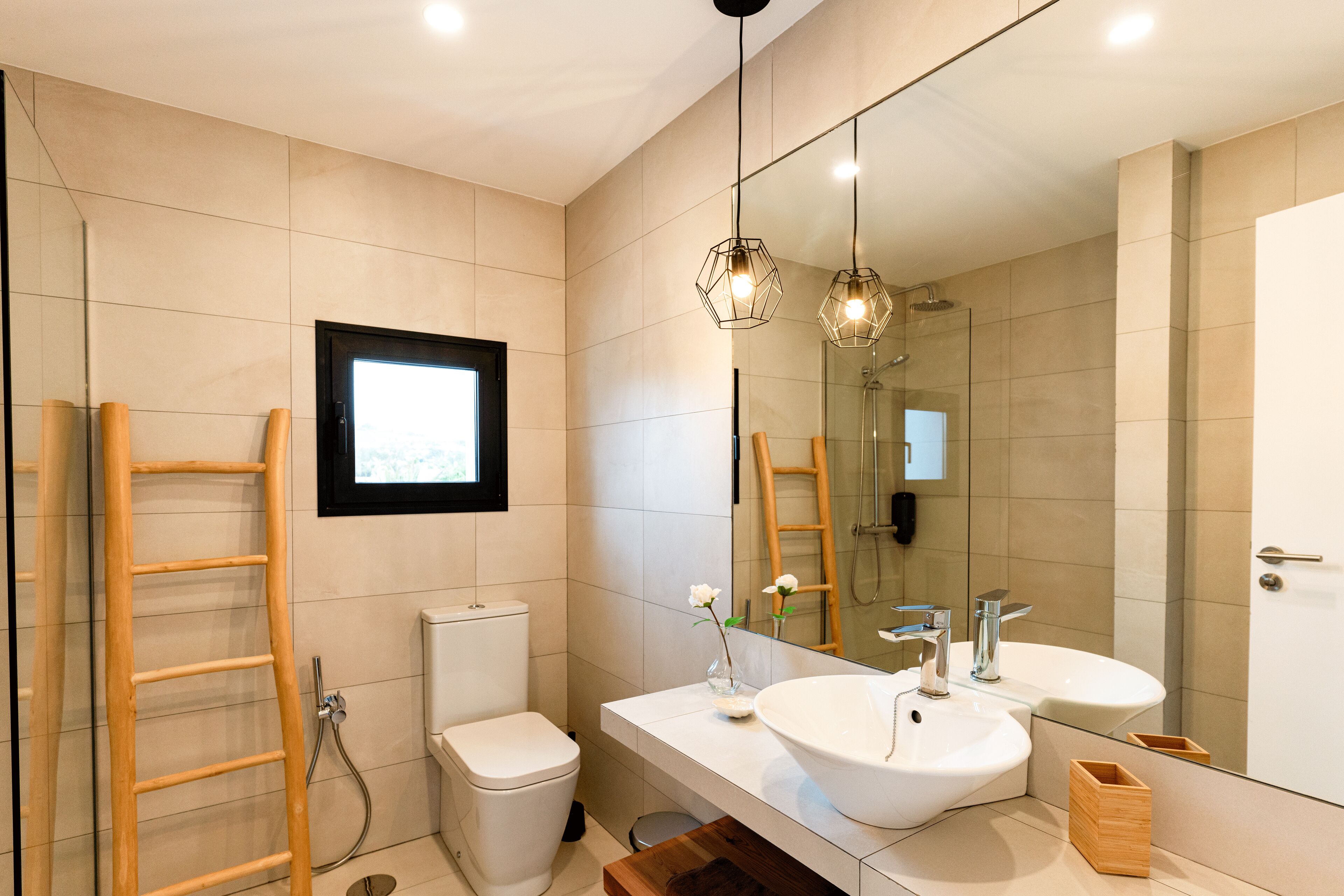 Un baño moderno con inodoro, bidé, dos lavamanos, un espejo grande y una escalera de madera.