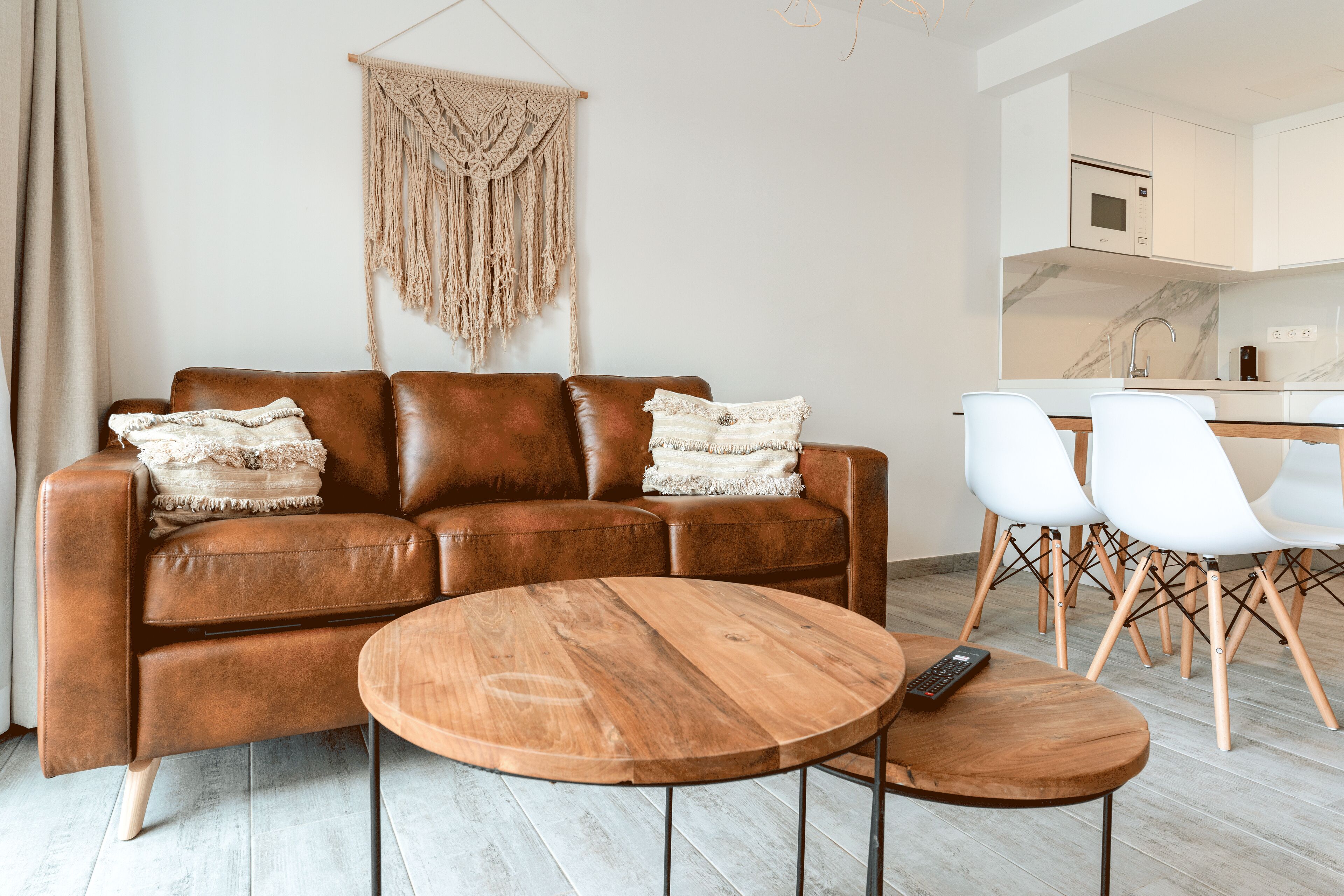 A modern living room with a brown leather sofa, a wooden coffee table, and a macrame wall hanging.