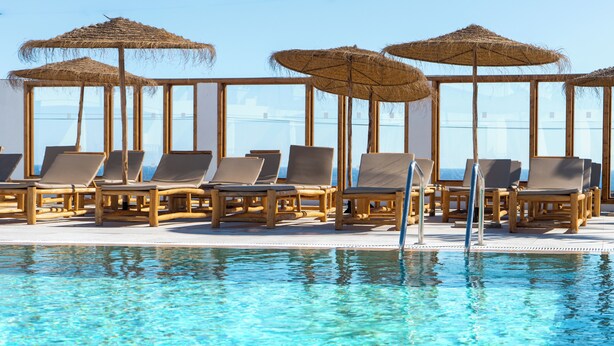 A poolside area with lounge chairs and thatched umbrellas, overlooking a clear blue pool. - Shambhala Fuerteventura (La Oliva)