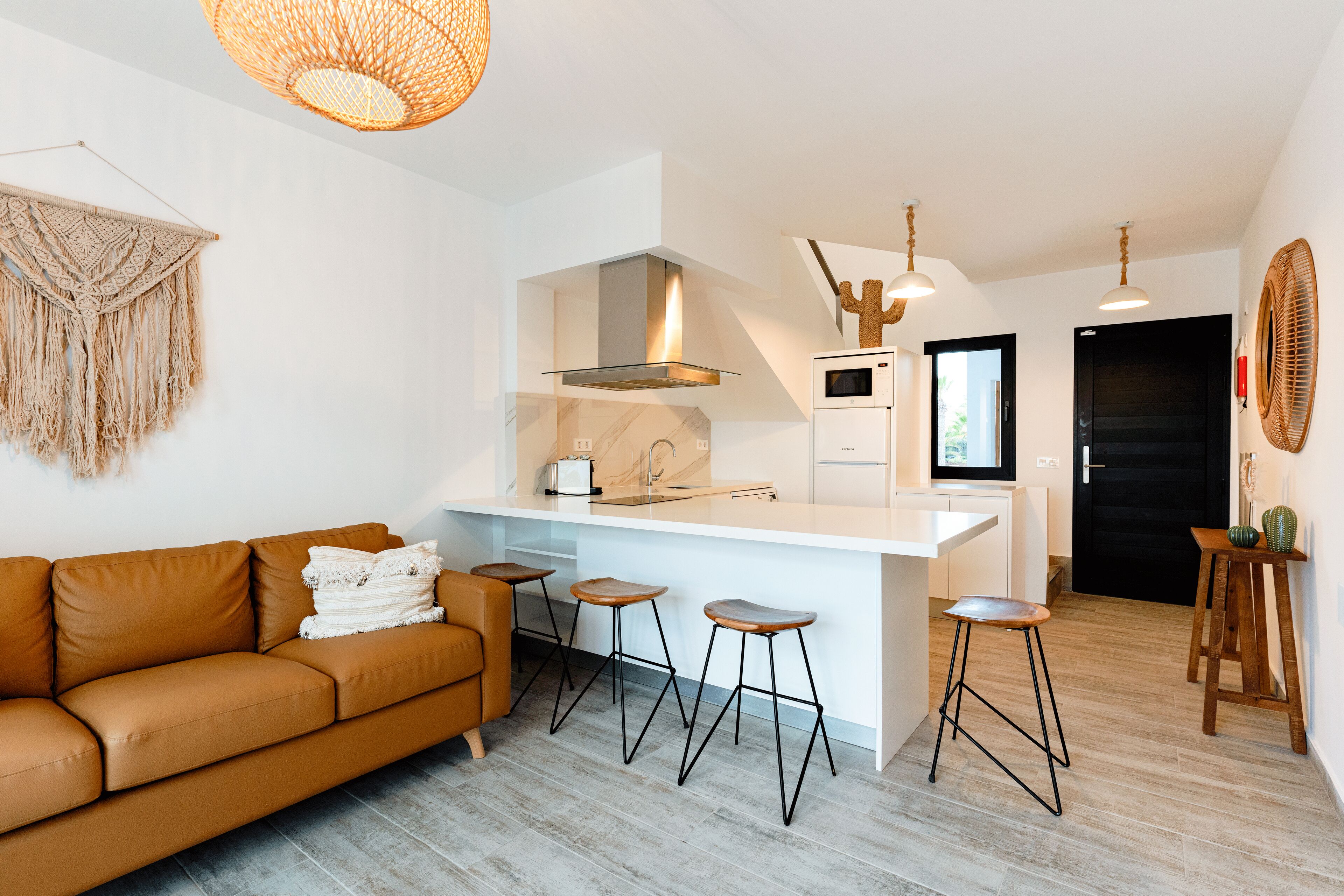 Et moderne køkken med en central ø, barstole og en brun lædersofa.