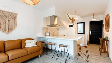 Et moderne køkken med en central ø, barstole og en brun lædersofa.