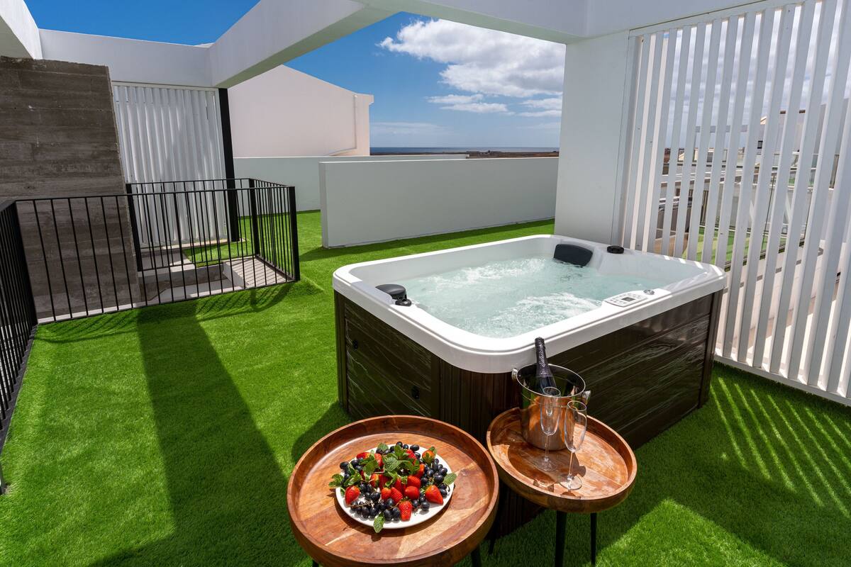 Een dakterras met een hottub, een houten tafel met een fruitschaal en een glas champagne.