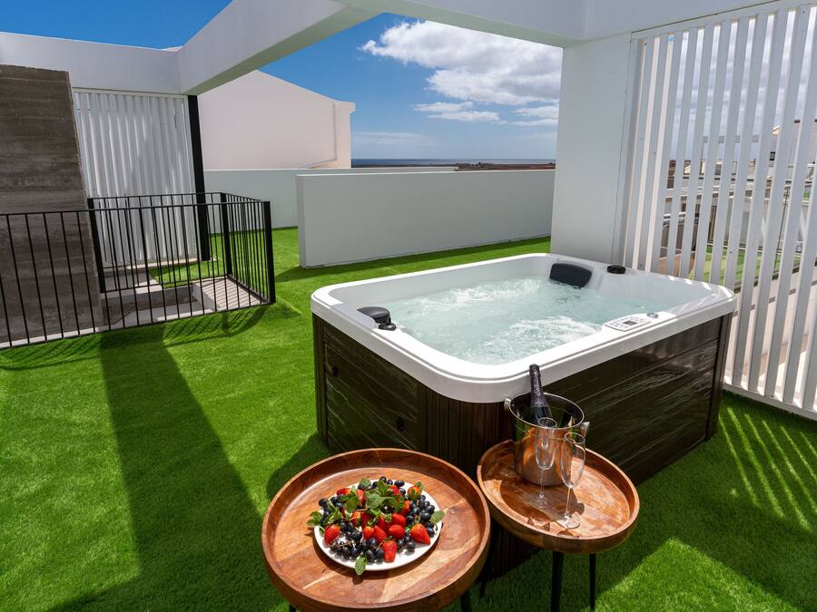 Une terrasse sur le toit avec un jacuzzi, une table en bois sur laquelle est posé un panier de fruits, et une coupe de champagne.
