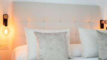 Un letto rifatto con testa imbottita, due cuscini e una lampada a parete.