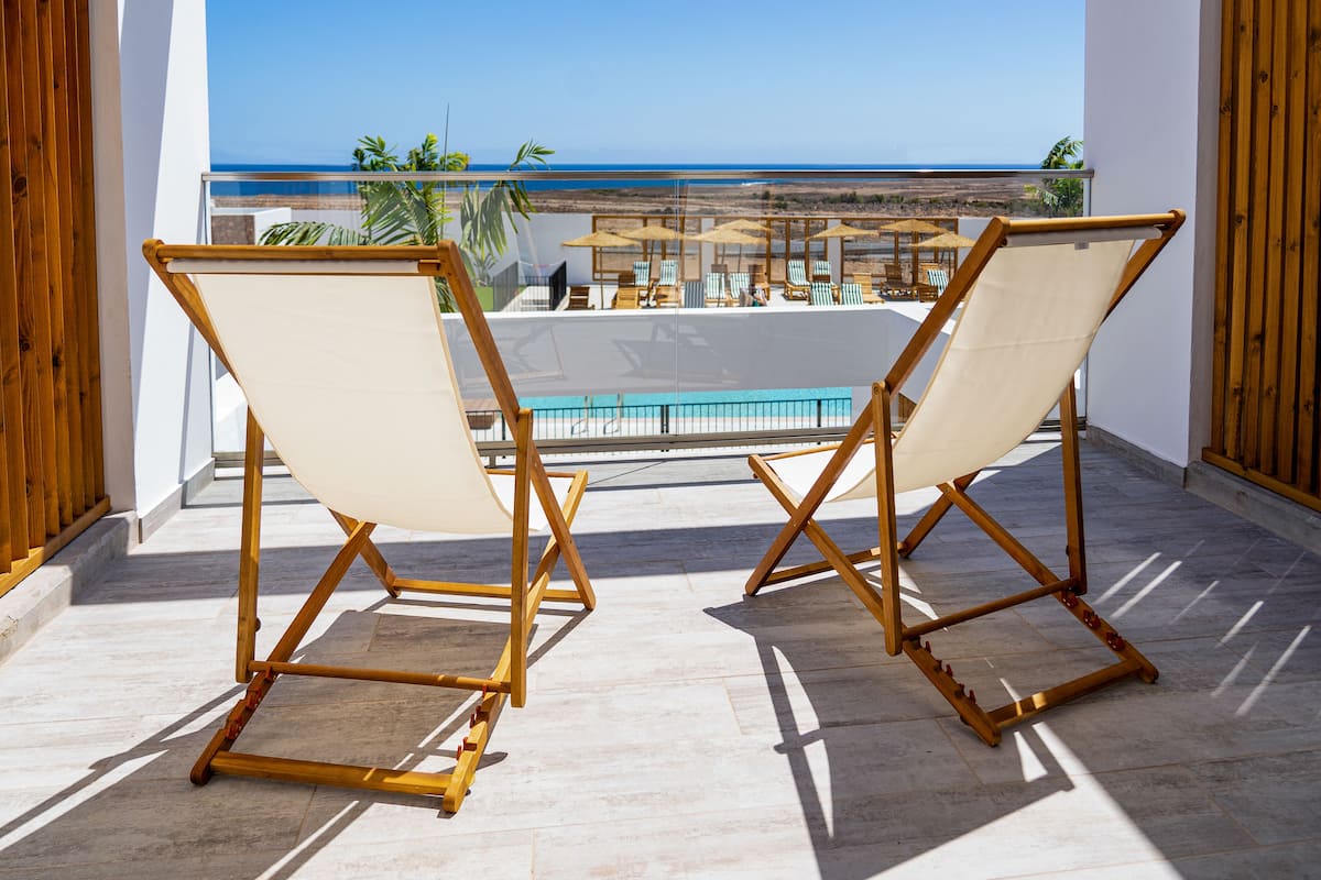 Twee houten stoelen met canvas ruggen bieden uitzicht op een zwembad en strand.