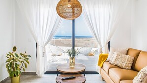 A room with a view of the beach, a sofa, a coffee table, and a hanging light fixture. - Shambhala Fuerteventura (La Oliva)
