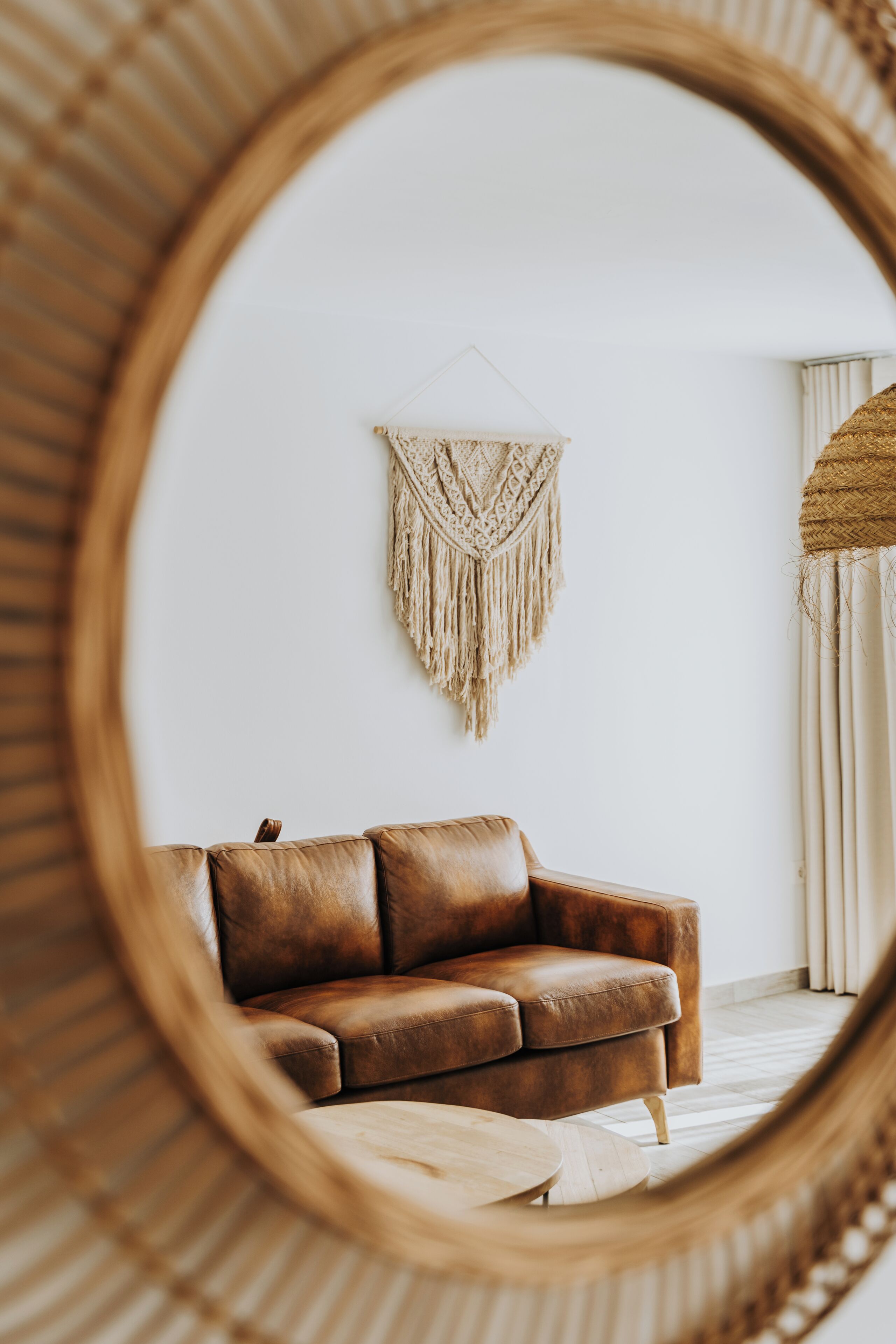 Una habitación con un sofá de cuero marrón, una mesa de centro redonda de madera y un tapiz de macramé en la pared.