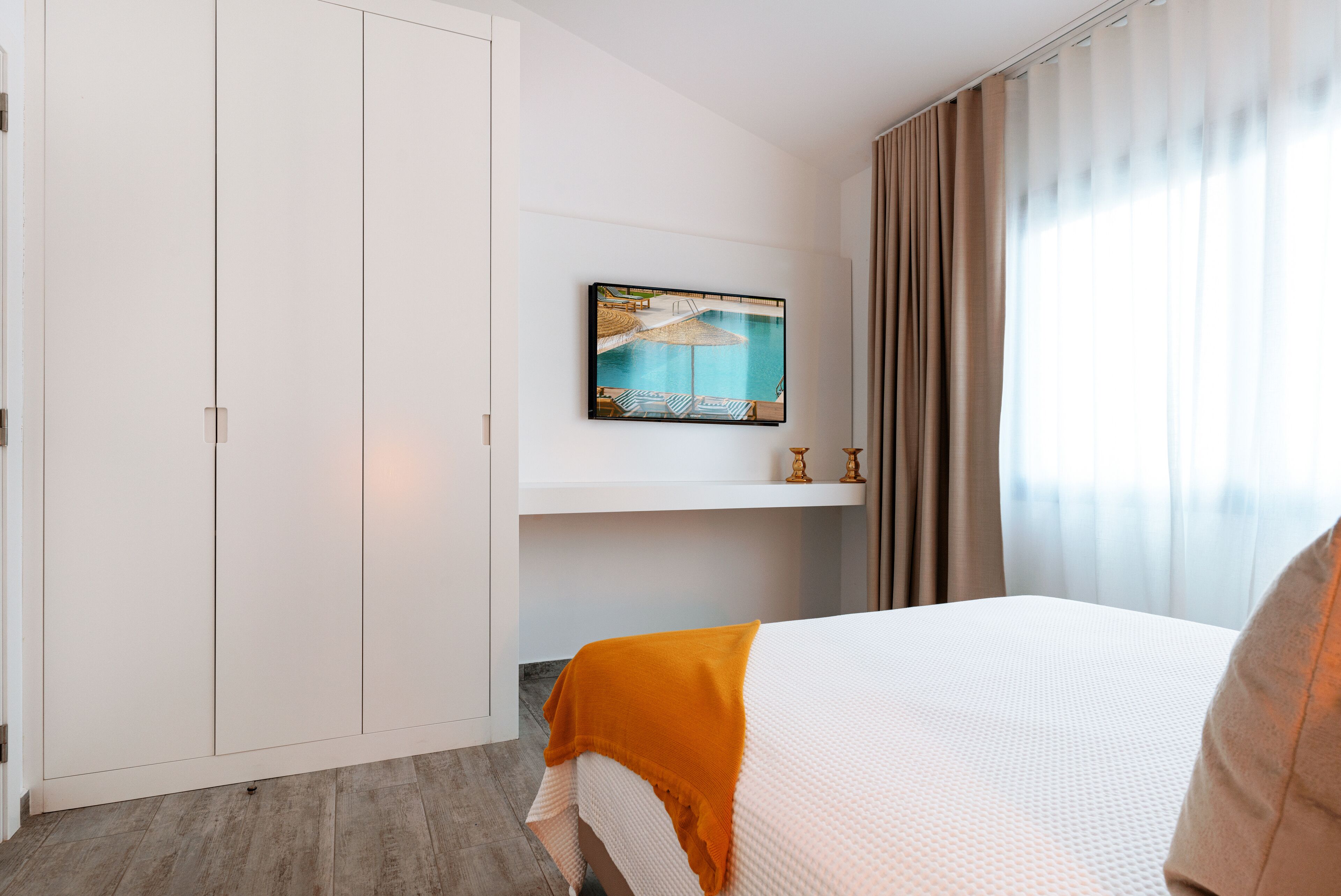 A hotel room with a bed, a painting of a beach scene, a wardrobe, and a window with curtains.