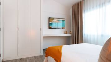 A hotel room with a bed, a painting of a beach scene, a wardrobe, and a window with curtains.
