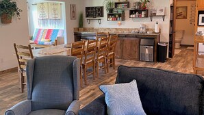Una sala moderna con un sillón gris, un sofá azul oscuro y un cojín estampado. Se ve un área de comedor con sillas de madera y una mesa al fondo.