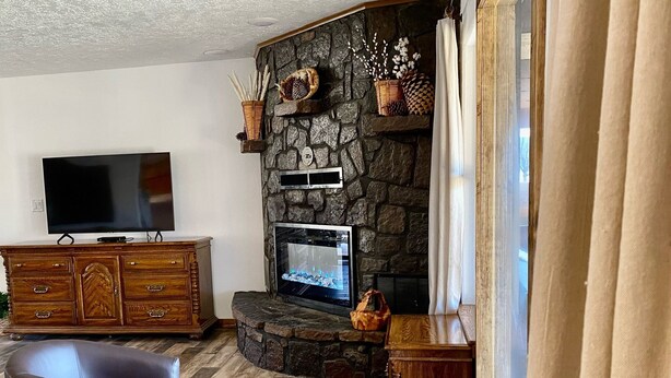 Un salon avec une cheminée en pierre, un téléviseur à écran plat, un meuble en bois et deux fauteuils en cuir.