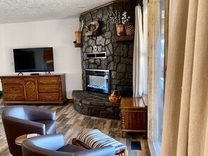 Una sala de estar con chimenea de piedra, un televisor de pantalla plana, un mueble de madera y dos sillones de cuero.