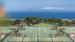 Complejo de canchas de tenis con varias pistas, rodeado de palmeras y vistas al océano.