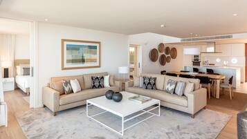 A modern living room with a beige sectional sofa, a white coffee table, and a dining area with a wooden table and chairs.
