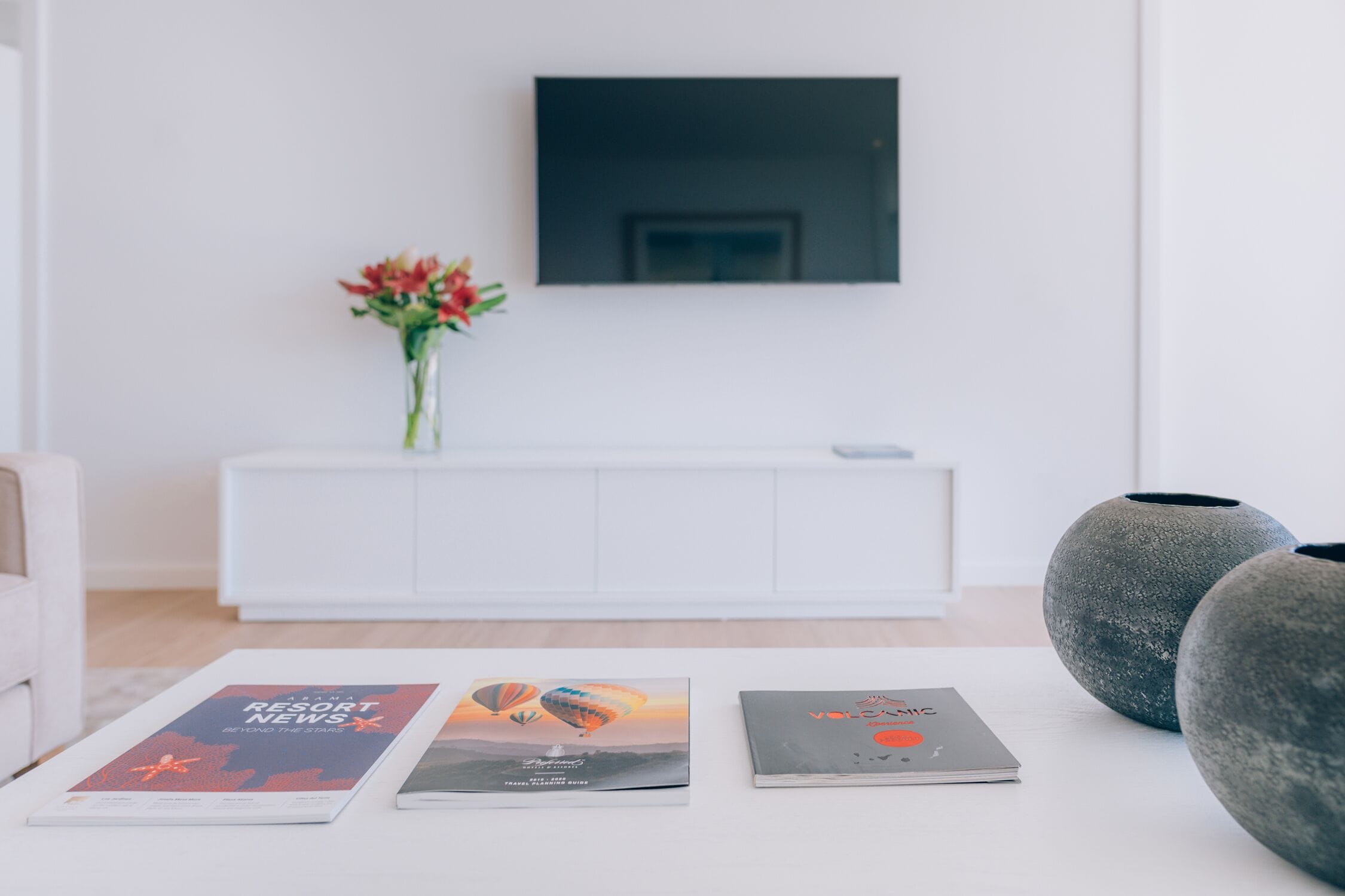 Una sala moderna con un sofá blanco, una consola blanca con un florero y un televisor de pantalla plana montado en la pared.