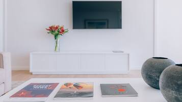 Una sala moderna con un sofá blanco, una consola blanca con un florero y un televisor de pantalla plana montado en la pared.