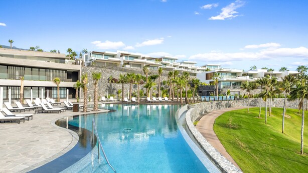 Un hotel moderno con piscina, tumbonas y palmeras.