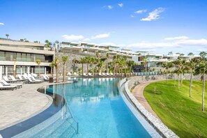 Un hotel moderno con piscina, tumbonas y palmeras.