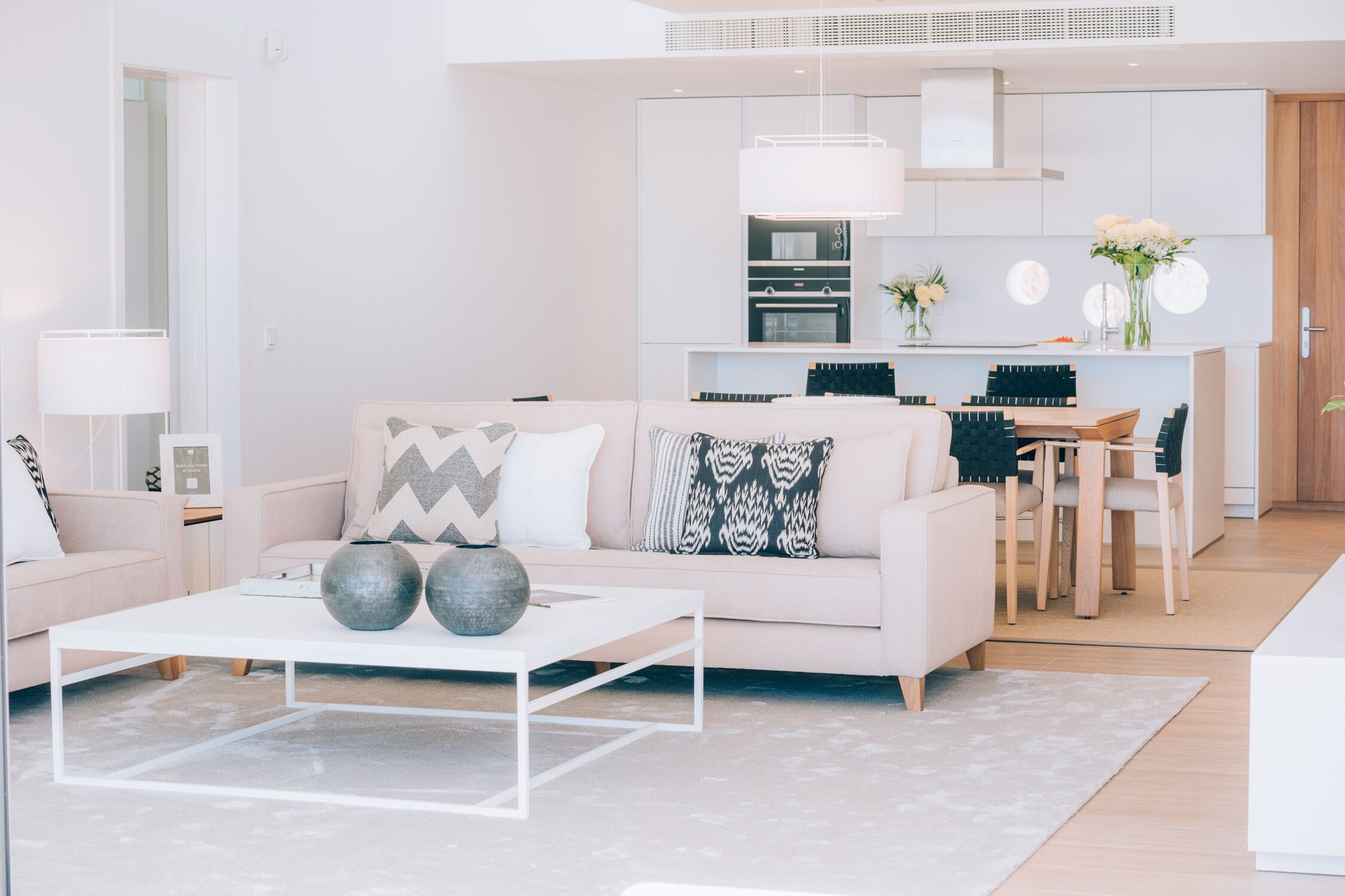 Una sala de estar moderna con un sofá blanco, una mesa de centro y una cocina al fondo.