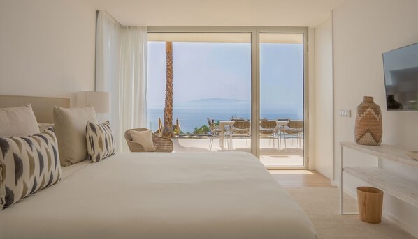 Un dormitorio con una cama grande, televisión y vista al mar a través de una puerta corrediza de vidrio.