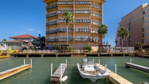 A multi-story hotel with balconies, a dock with a boat, and palm trees. - Amazing Bay View, Boat docks, and easy walk to the beach (South Padre Island)