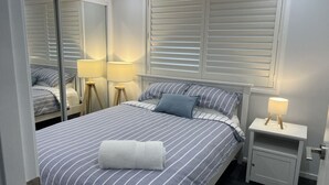 Une chambre à coucher bien rangée, avec un grand lit, deux lampes de chevet, un miroir et une table de chevet.