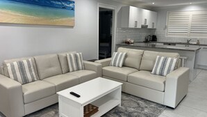 Un salon moderne avec un ensemble de canapés beige, une table basse blanche et un tableau représentant une scène de plage.