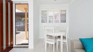 Une pièce comprenant une table à manger et des chaises, un canapé et une fenêtre avec des stores.