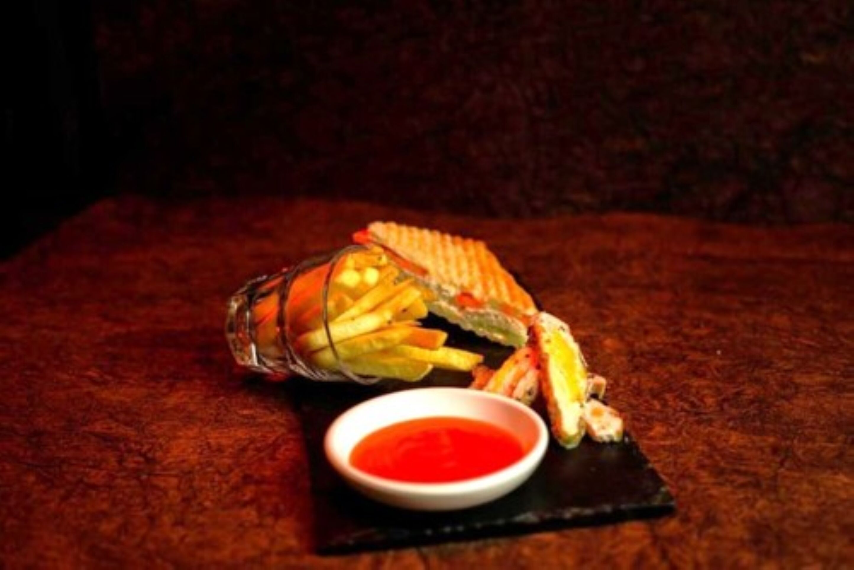 A sandwich and fries on a black slate with a red sauce.