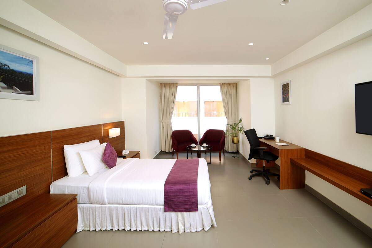 Habitación de hotel con cama, escritorio, sillas y televisor.