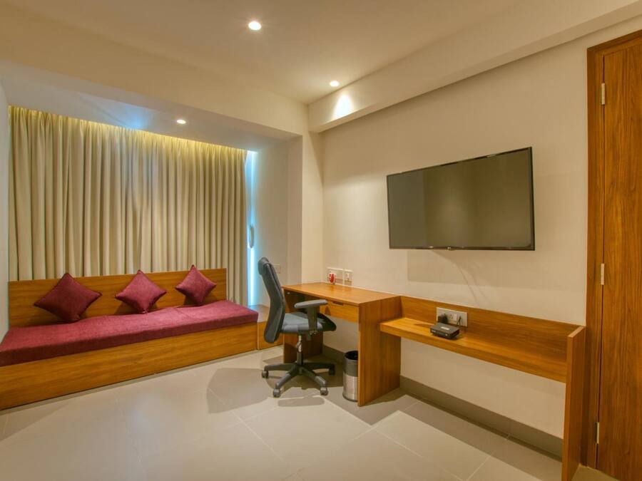 A modern room with a wooden desk, a comfortable sofa with cushions, a mounted TV, and a curtain-covered window.