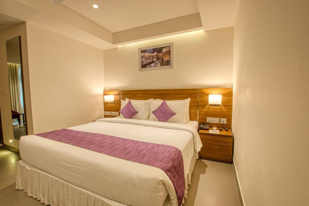 Una habitación de hotel con una cama grande, cabecera de madera, dos lámparas de noche y un cuadro en la pared.