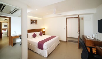 A hotel room with a bed, desk, chair, and a door leading to another room.