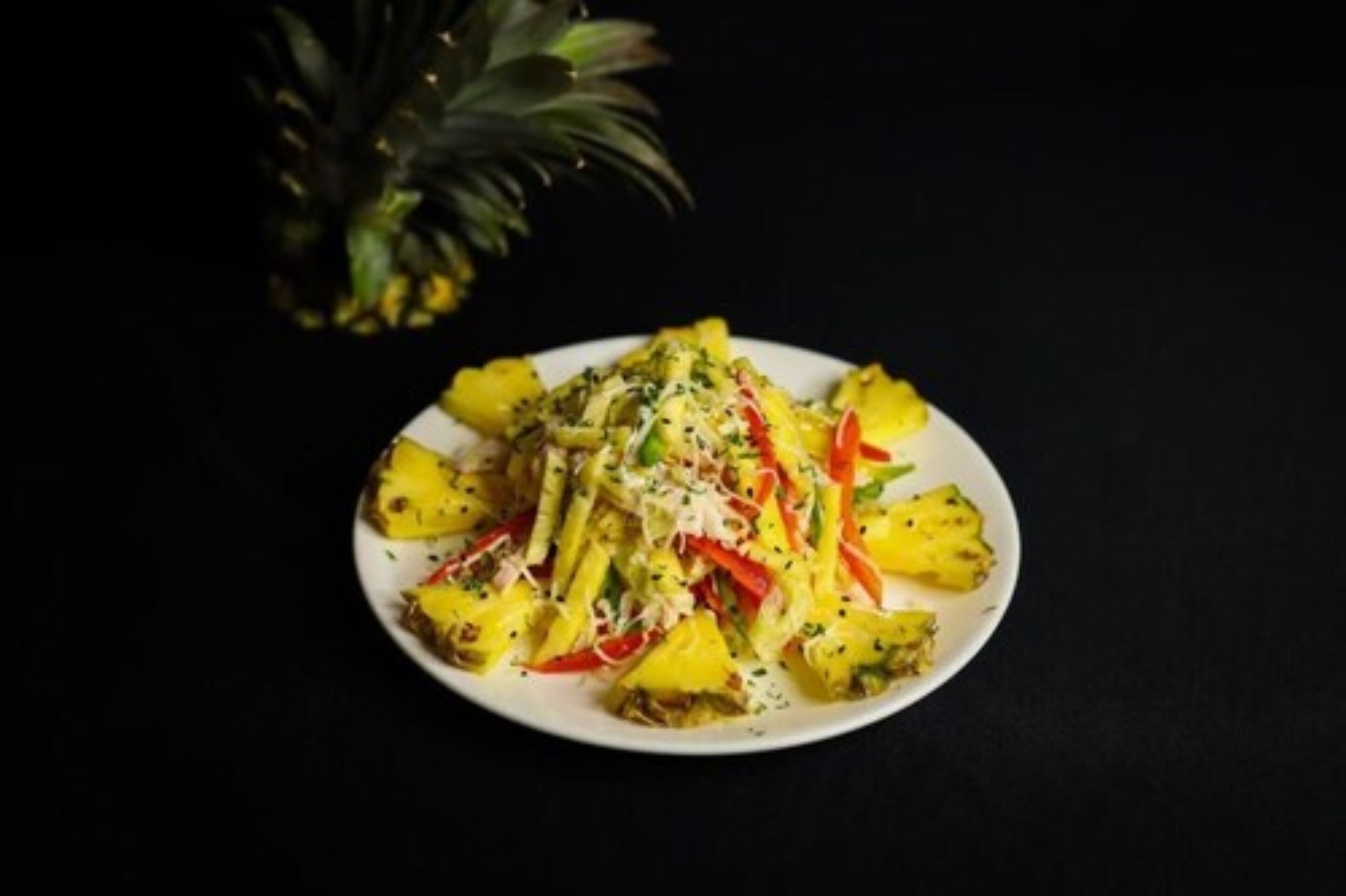 Un plato de comida con trozos de piña, pimientos rojos y hierbas aromáticas.