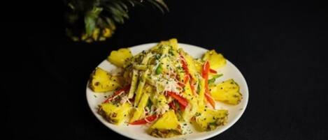 A plate of food with pineapple chunks, red bell peppers, and herbs.