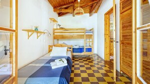 A compact room with a bunk bed, a single bed, a checkered floor, wooden walls, and a ceiling with exposed beams.