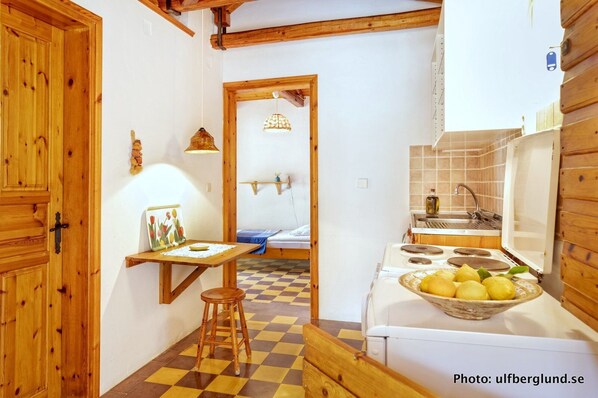 Cocina compacta con estufa, lavamanos y un pequeño comedor con mesa y taburetes.