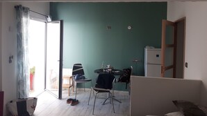 A room with a dining table, chairs, a refrigerator, and a bed.