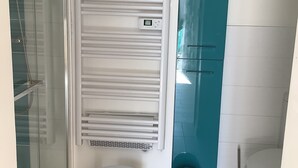 A bathroom with a glass shower enclosure, a white toilet, a blue cabinet, and a small white table.