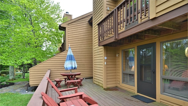 A wooden deck with a picnic table and benches, a blue umbrella, and a glass door with blinds.